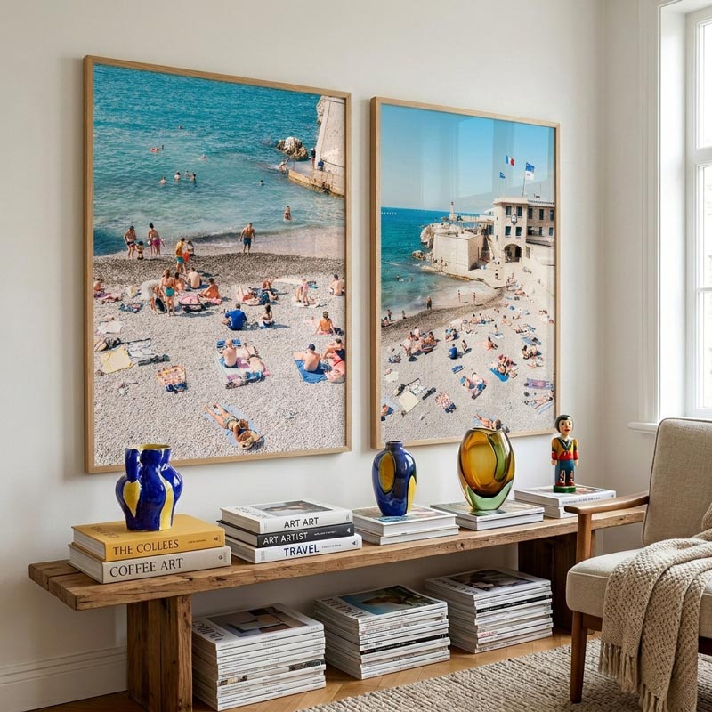 Two framed beach scenes on a wall above a wooden console table with decorative items.