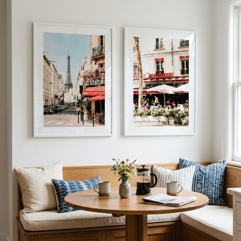 Two framed pictures of cityscapes above a wooden table with a coffee set in a cozy room.