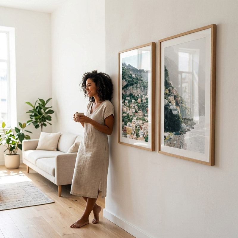 Woman standing in a living room with two framed landscape pictures on the wall.