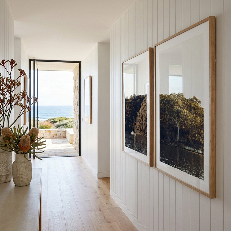 Modern interior with framed artwork on a white paneled wall, leading to an outdoor view.