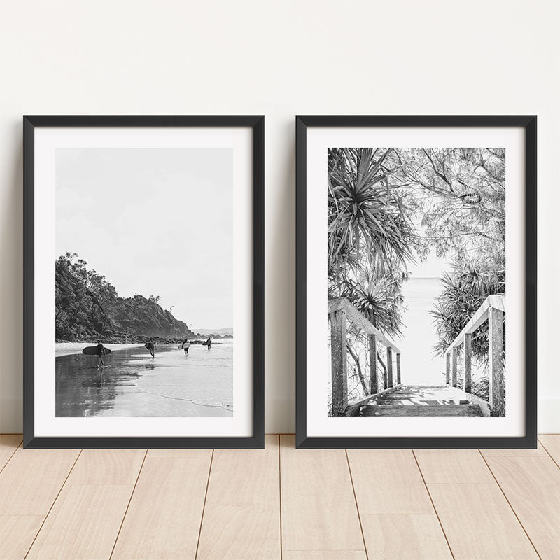 Two framed prints on a wooden floor, one black and white beach scene and the other a nature scene with a bridge.
