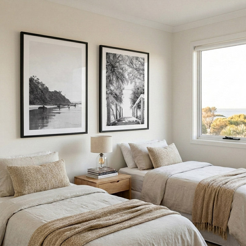 Neatly made bed with beige bedding in a bedroom with framed artwork on the wall.