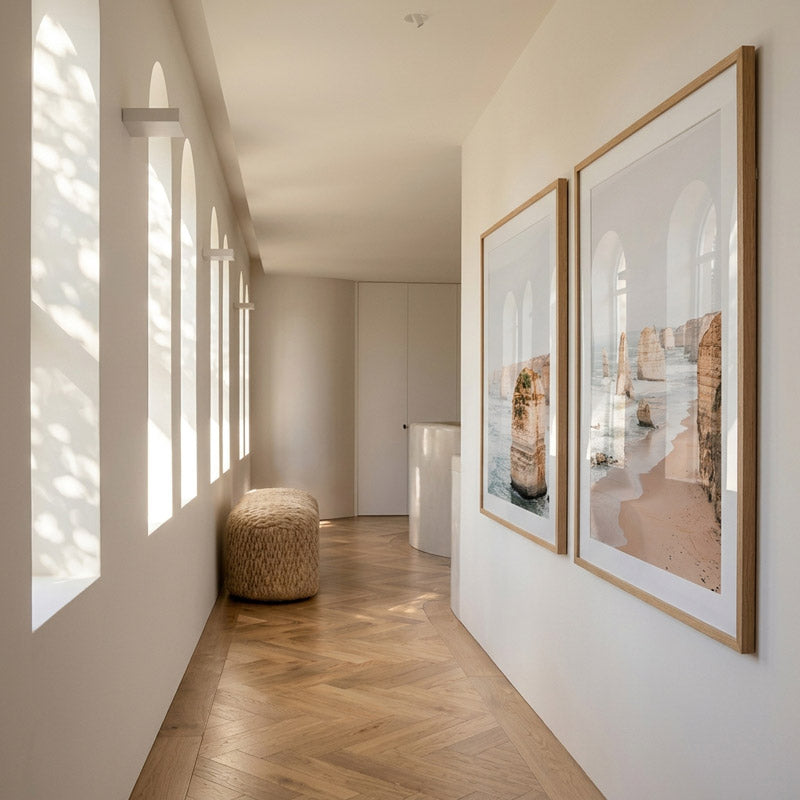 Modern interior with two framed artworks on a wall, sunlight filtering through windows.