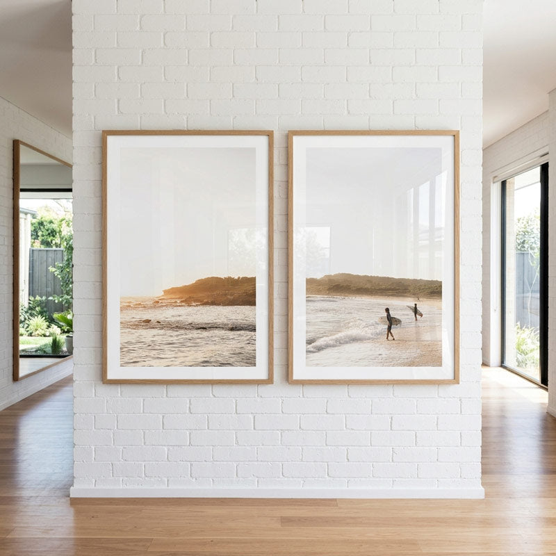 Two framed beach scenes on a white brick wall in a modern interior.