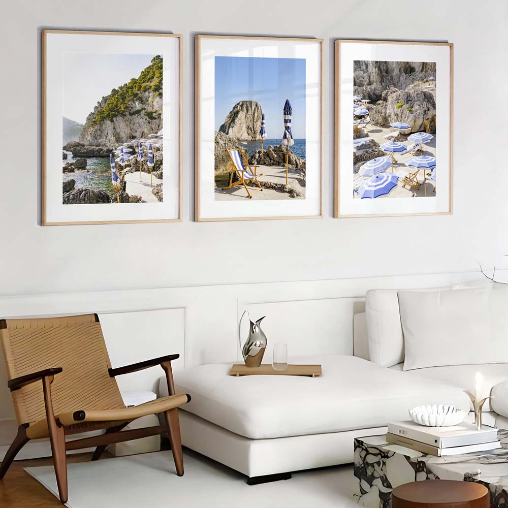 A set of three framed photographs on a wall depicting coastal scenes with rocks and a lighthouse.
