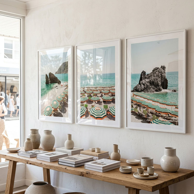 Three framed beach scenes above a wooden table with decorative items.