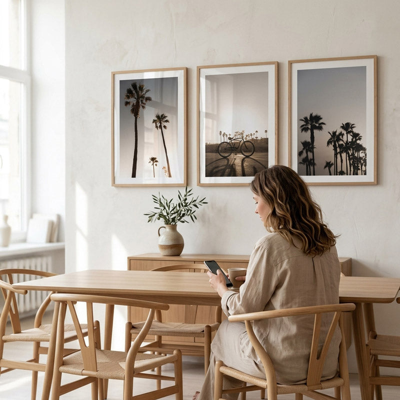 Woman sitting at a wooden table in a modern dining room with palm tree-themed artwork on the wall.