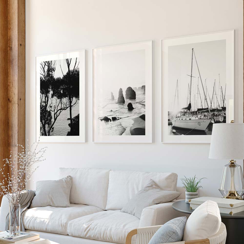 A set of three black and white photographs in picture frames, depicting marine scenes with boats and natural elements, displayed on a wall above a white sofa.