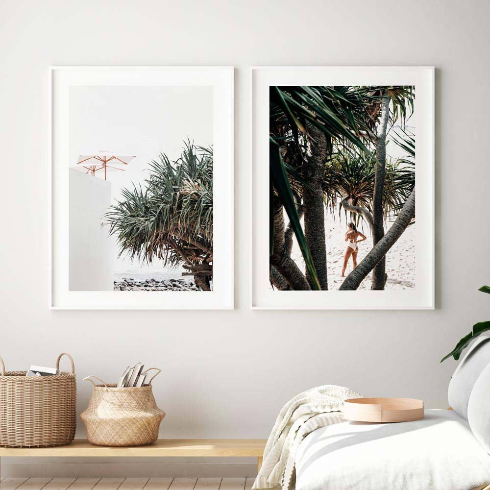 Two framed prints hanging on a wall, featuring beach scenes with palm trees and a person wading in the water.
