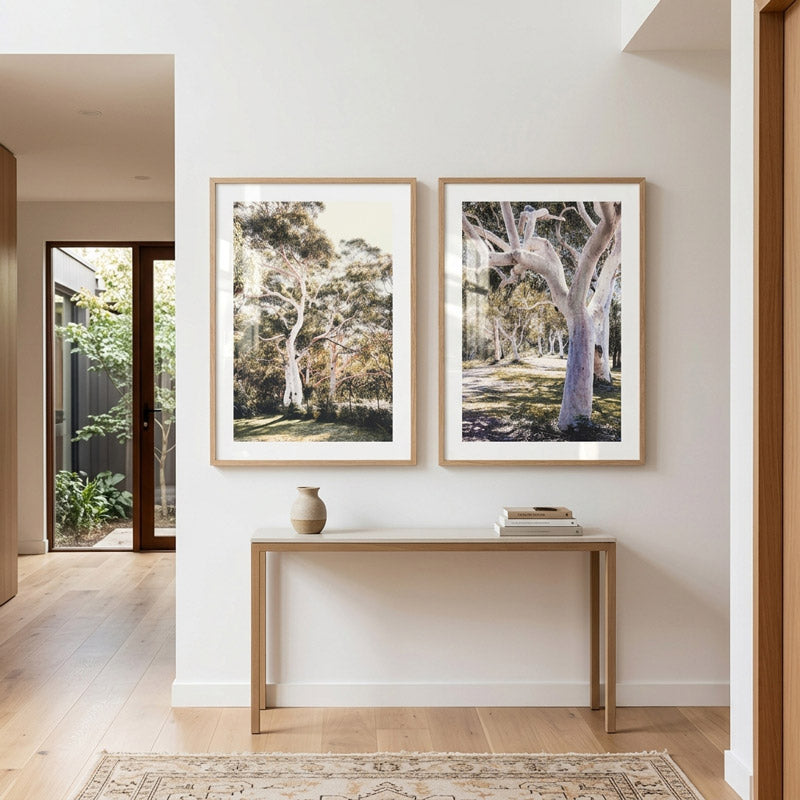 Two framed tree pictures on a wall above a console table in a room with a door and rug.