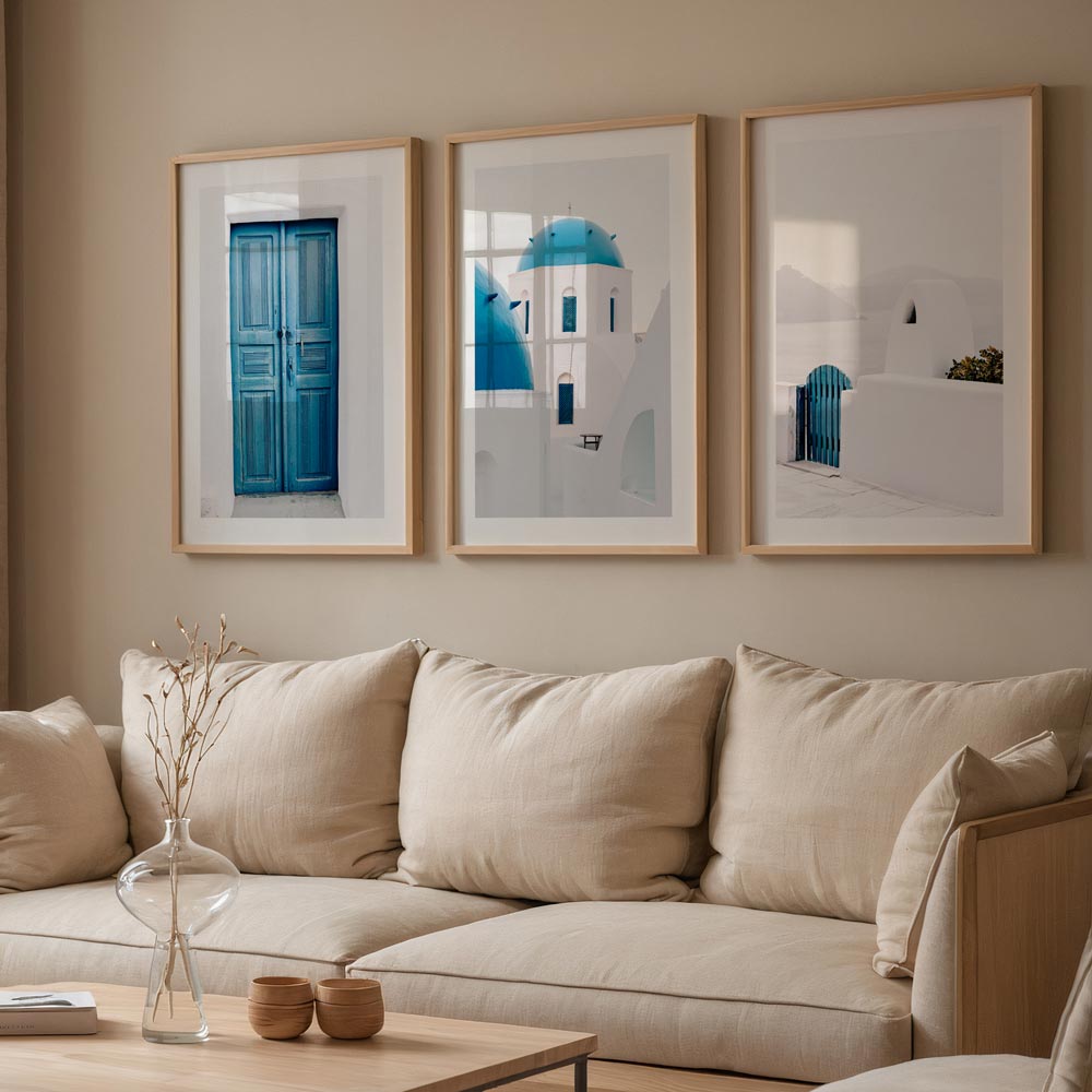 A set of three framed horizontal photographs with blue and white doorways and gates, displayed on a wall above a beige sofa.