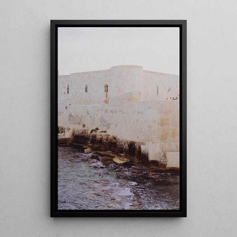 Framed photograph of a stone wall with water below on a light gray wall.