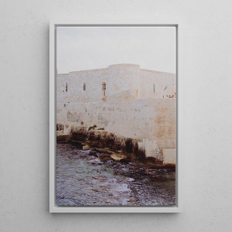 Framed photograph of a stone wall with water below on a light gray wall.