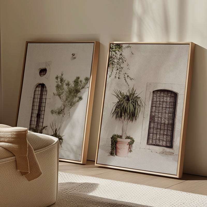 Two framed artworks of plants and architectural elements on a wall with a beige armchair.