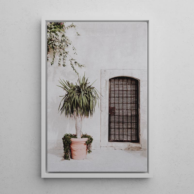 Framed print of a potted plant in front of a textured wall with a window.