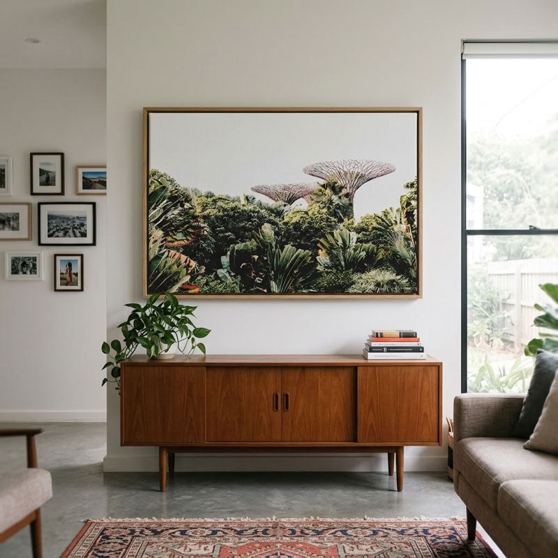 A large framed landscape art print depicting lush green tropical foliage and distinctive mushroom-like trees, styled in a mid-century modern living room above a wooden sideboard.