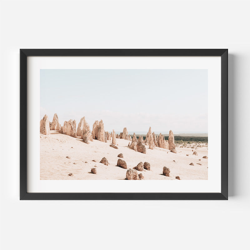 Framed photograph of rock formations in a desert landscape on a white wall.