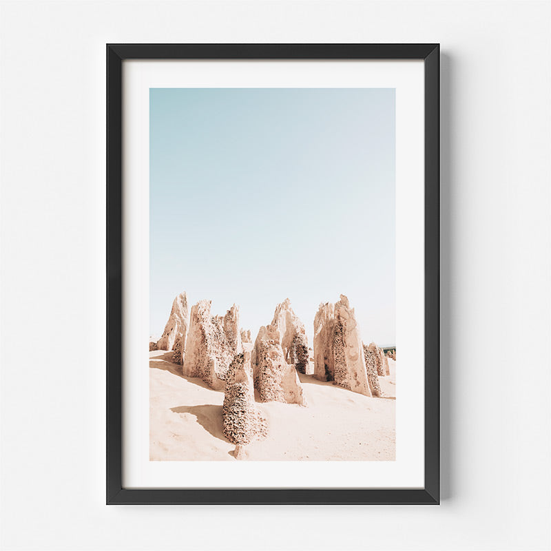 Framed artwork of desert landscape with rock formations against a blue sky.