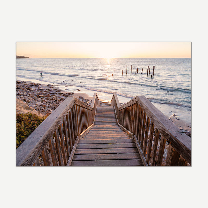Wooden staircase leading to a beach with sunset over water