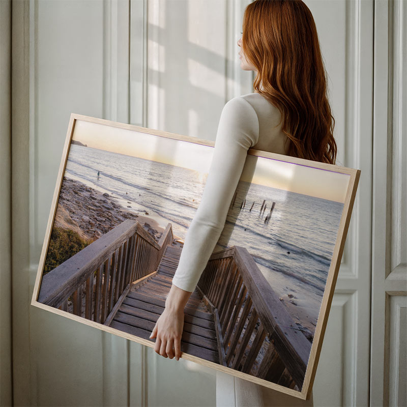 Woman holding a large framed picture of a beach scene