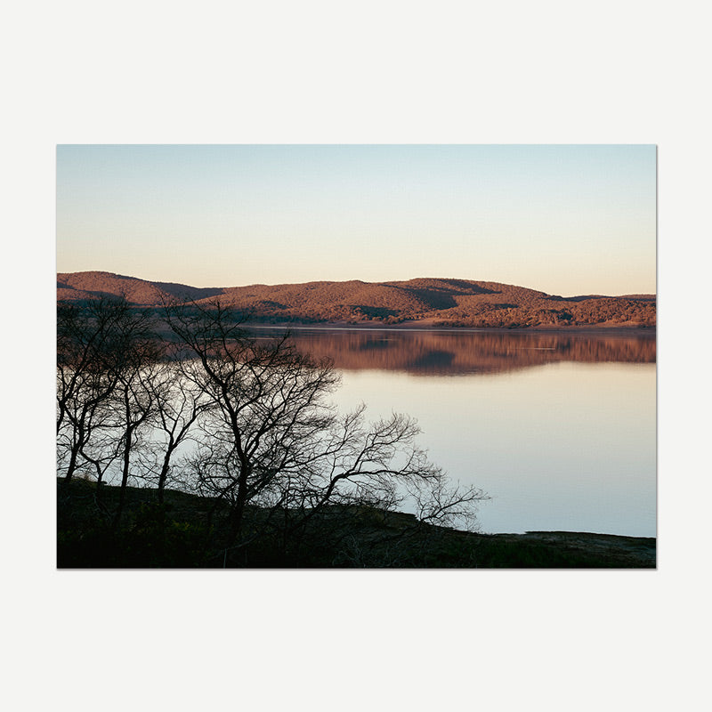 Silhouette of trees by a lake with mountains in the background