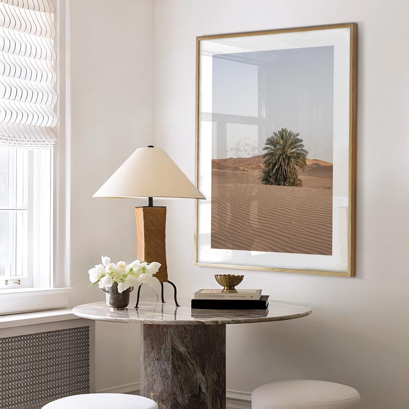 Modern interior with a table, lamp, and framed desert landscape art on a white wall.