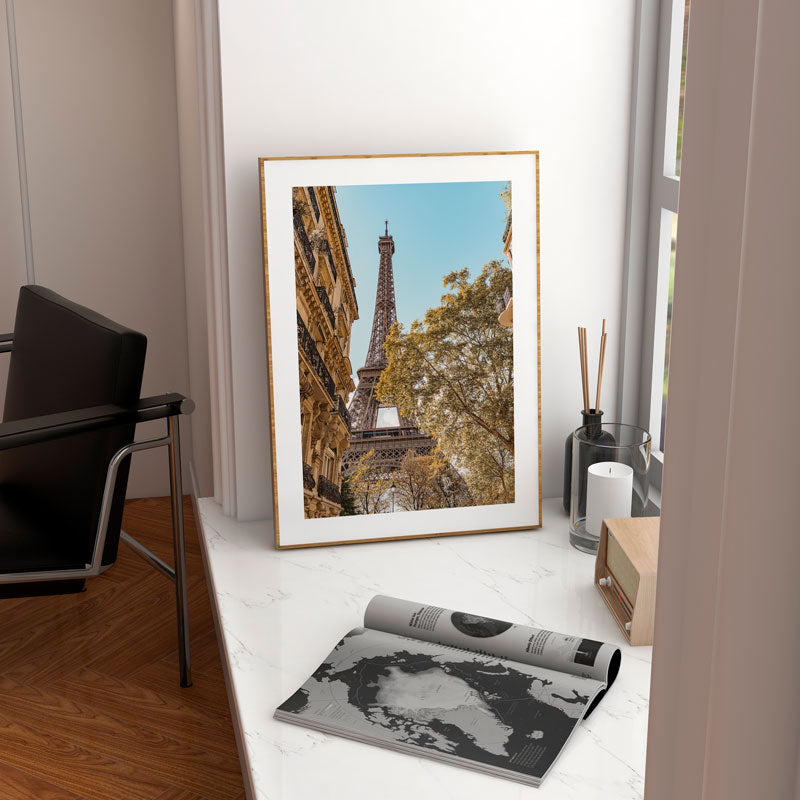Framed picture of the Eiffel Tower on a white surface with a candle and diffuser in the background.