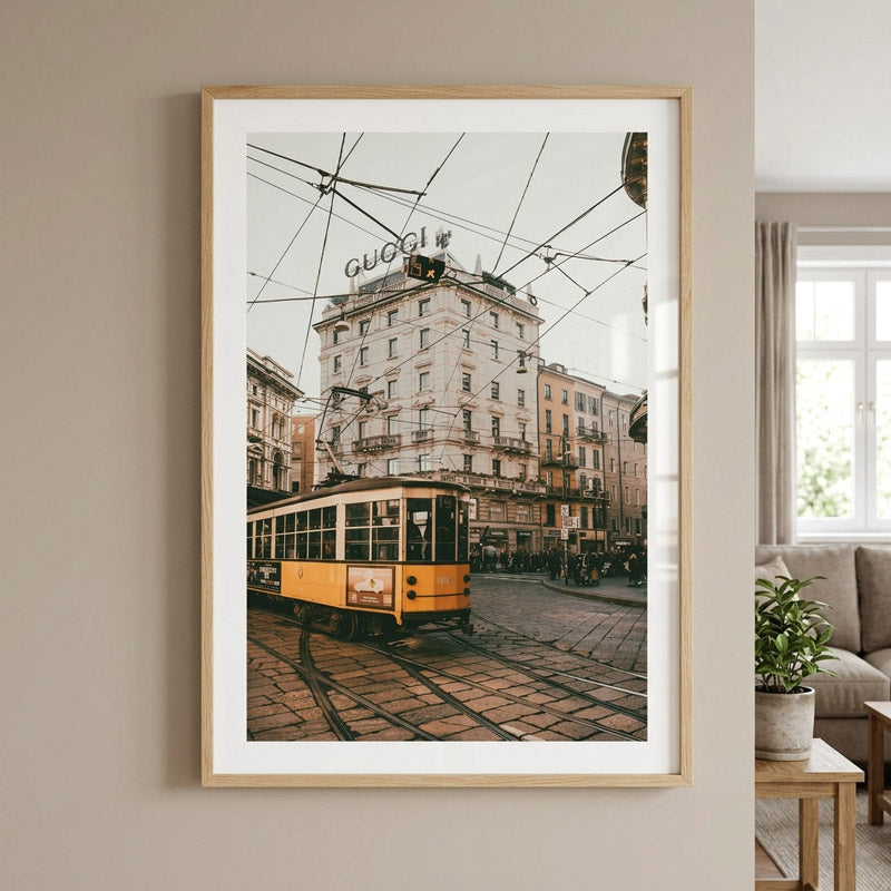 A framed art print featuring a vintage yellow tram on a cobblestone street in front of an old building with a visible 'GUCCI' sign, displayed on a beige wall in a modern living room setting.
