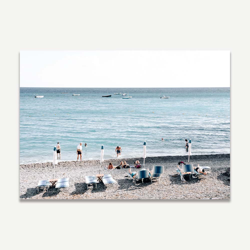 Wall art of Fornillo Beach with sunbeds, beachgoers, black sand, and the blue Mediterranean Sea in soft afternoon light.