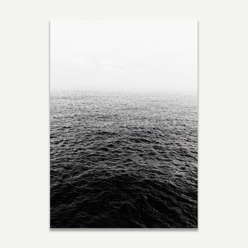 A black and white photo of a calm ocean horizon with a misty or stormy sky above.