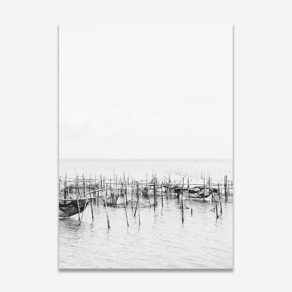 A black and white photograph of a fishing village with fishing nets and wooden posts, shown as print
