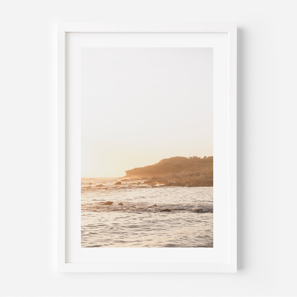 A white framed photograph of the ocean and waves at sunrise, perfect for wall art decor.