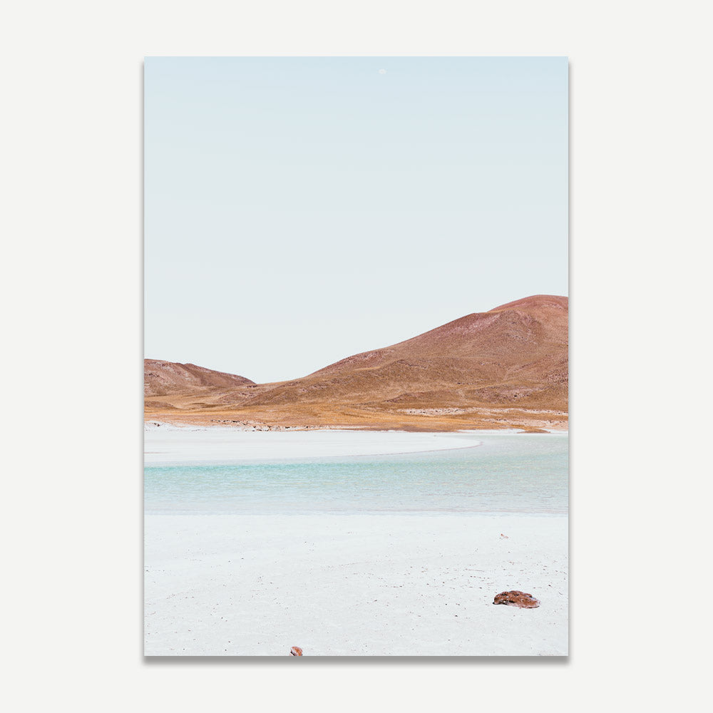 A landscape photograph featuring a remote desert scene with hills in the background and a clear sky, predominantly in shades of blue, orange, and white.