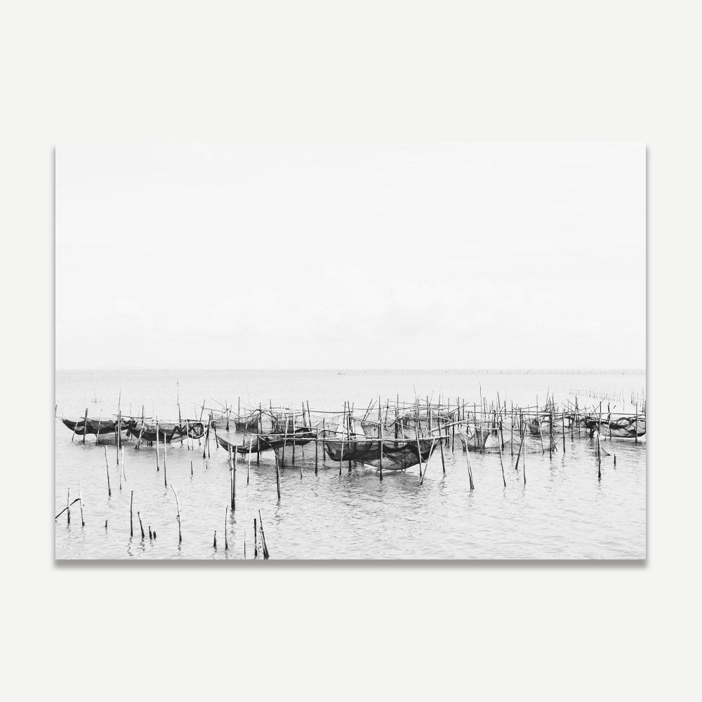 Black and white photograph of a fishing village in Thailand, featuring fishing nets and wooden posts in a monochrome setting.