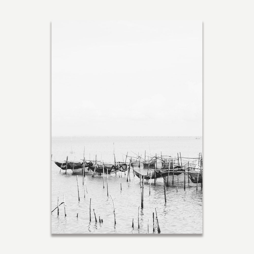 A black and white photograph of fishing nets and wooden posts in water, likely taken in a Thai fishing village, displayed as print