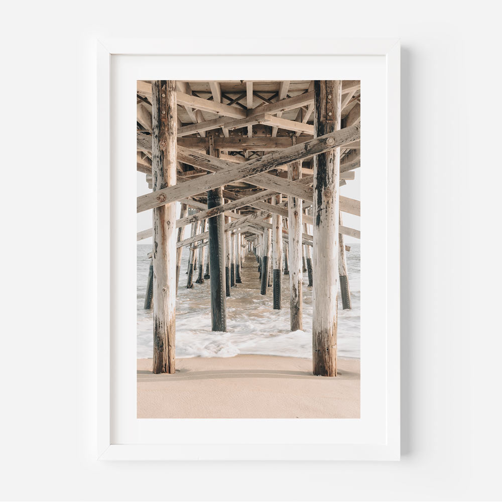 A white framed photo of the ocean under a pier. Wall art decor capturing the beauty of the California coast.