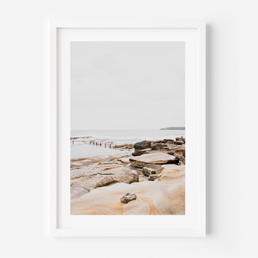 A white framed photo captures the serene beauty of an ocean and rocks at Mahon Pool, Maroubra - wall art decor by Oblongshop.